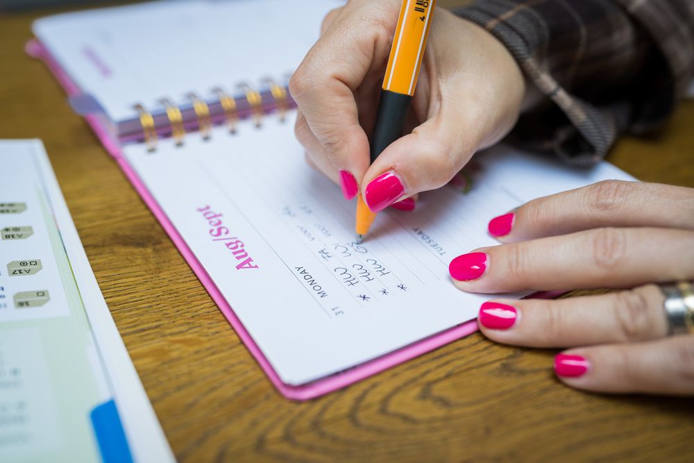 Close-up van een hand die een planning in een agenda schrijft