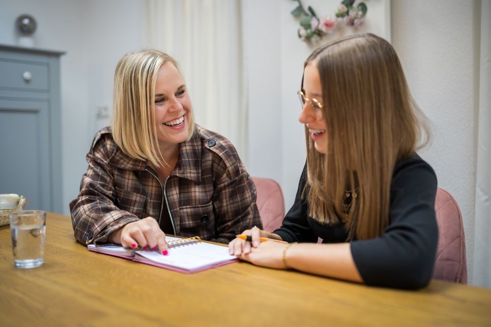 Suzanne en een leerling lachen samen boven een opengeslagen agenda