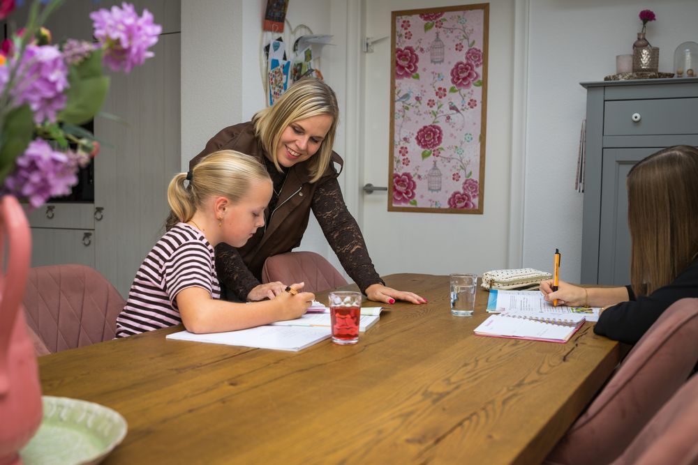 Suzanne buigt zich over de tafel naar een leerling die aan het werk is